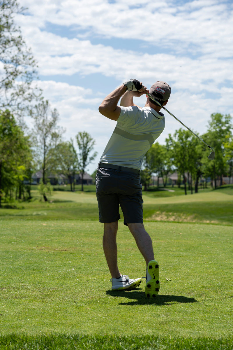 Man playing golf on a green course with trees and blue sky in the background