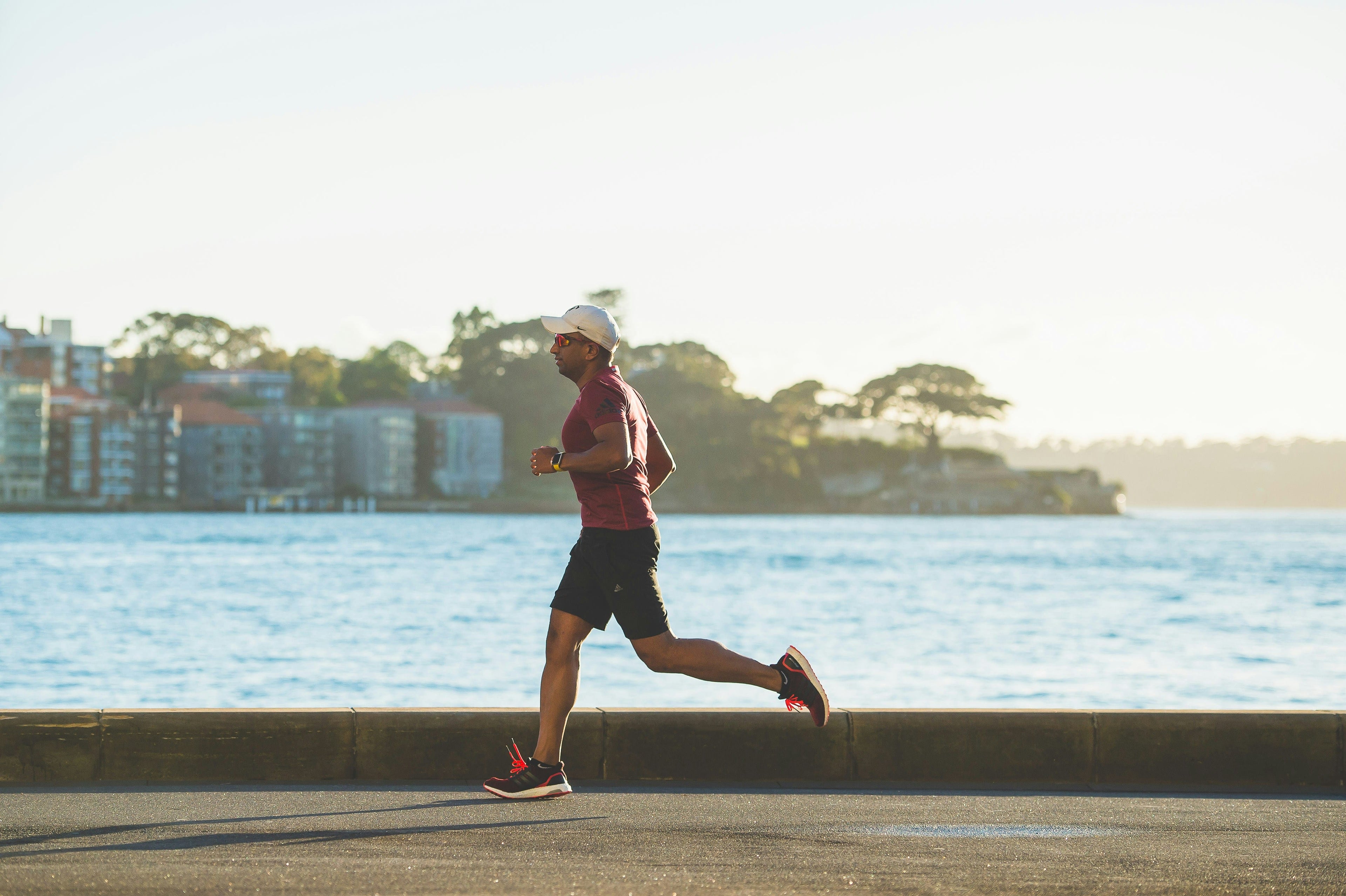 Man running by a waterfront with buildings and trees in the background