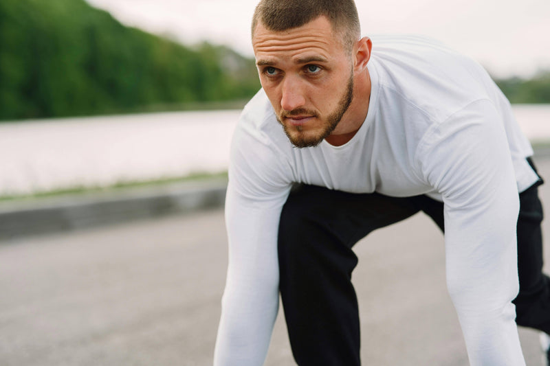 Man in athletic wear preparing to run outdoors with a blurred natural background