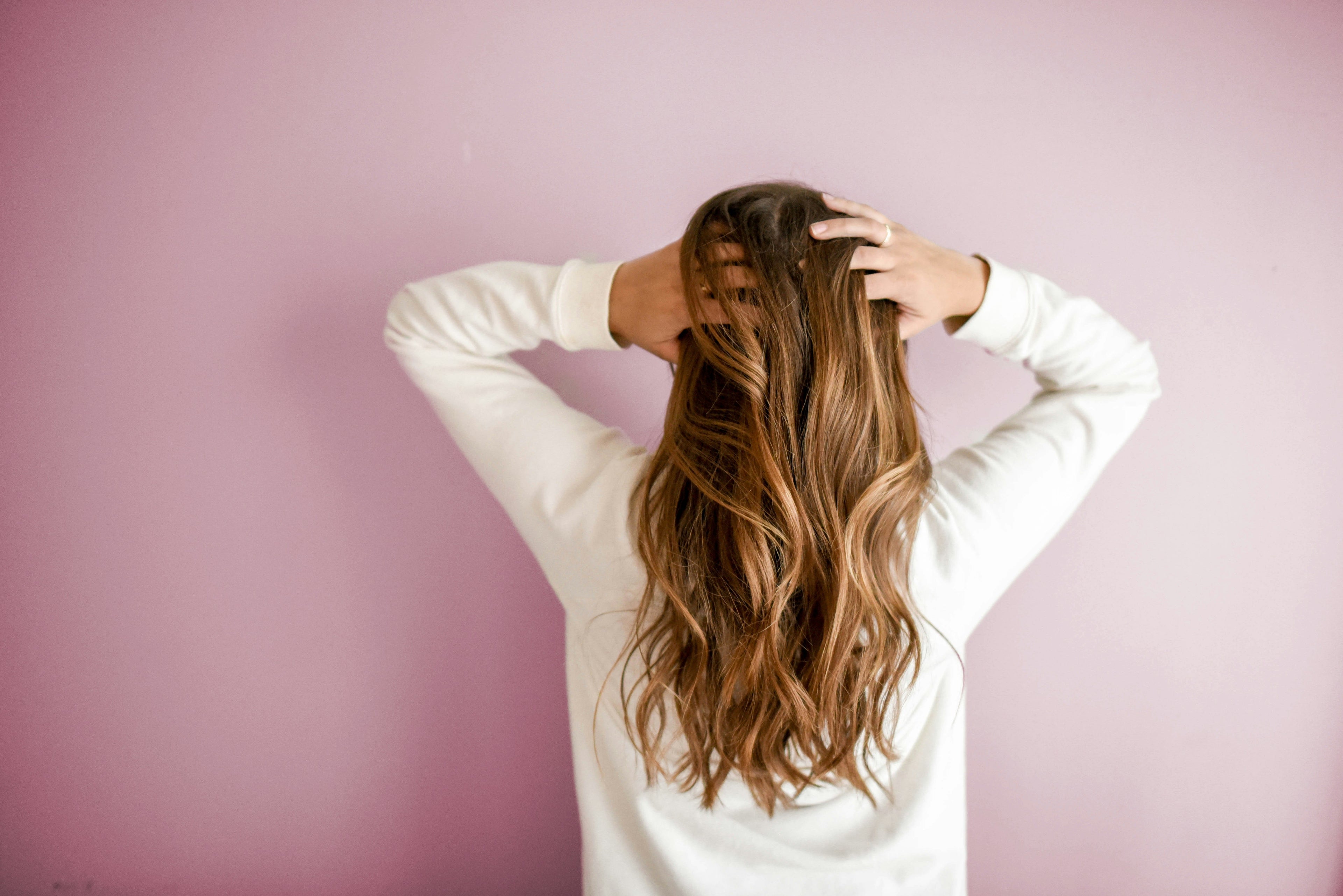 Person running their hands through their hair against a pink background