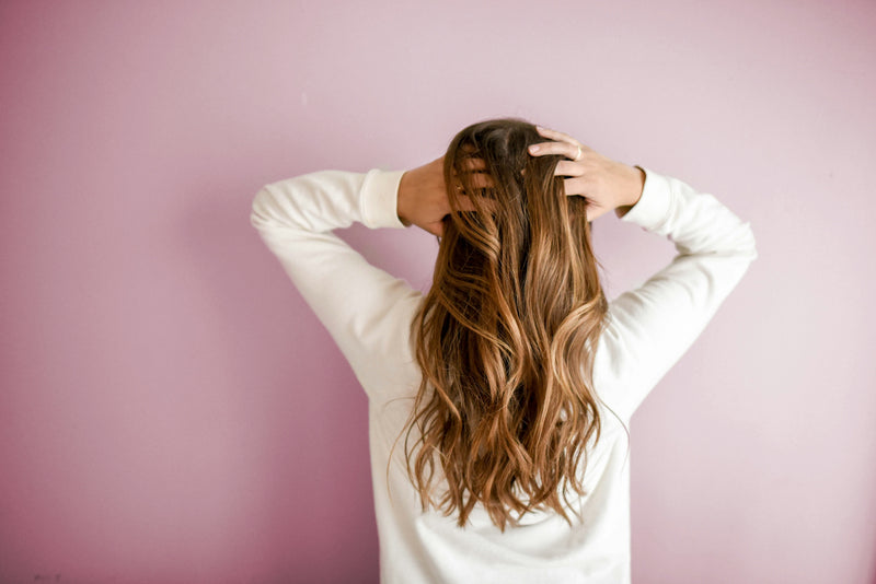 Person running their hands through their hair against a pink background